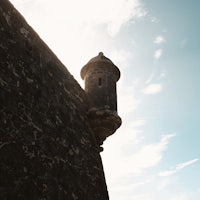 a man is flying a kite over a stone wall